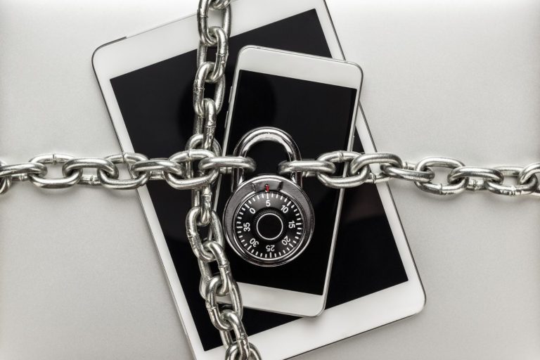 Ein Vorhängeschloss und Ketten um zwei elektronische Geräte auf einem Tisch.